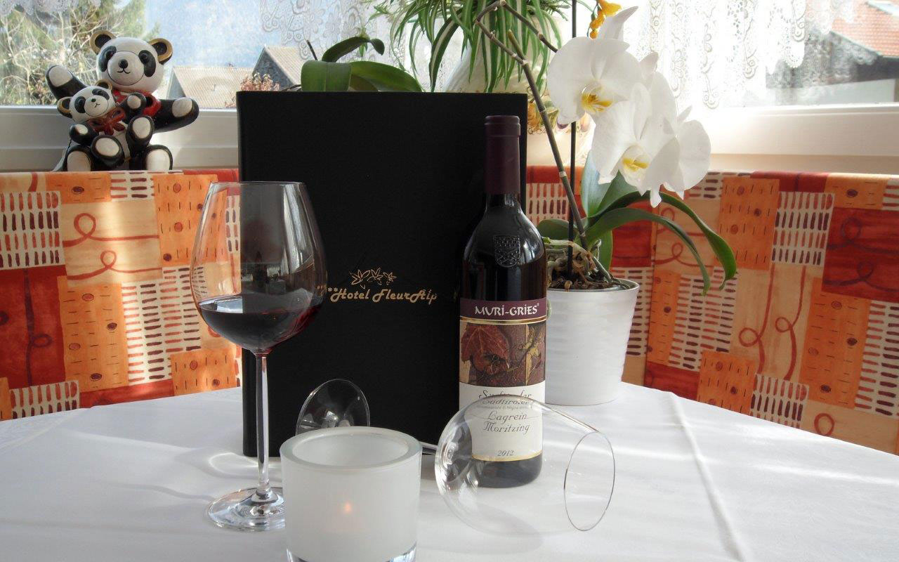 Carta dei vini appoggiata al tavolo con bottiglia di vino Lagrein e calici